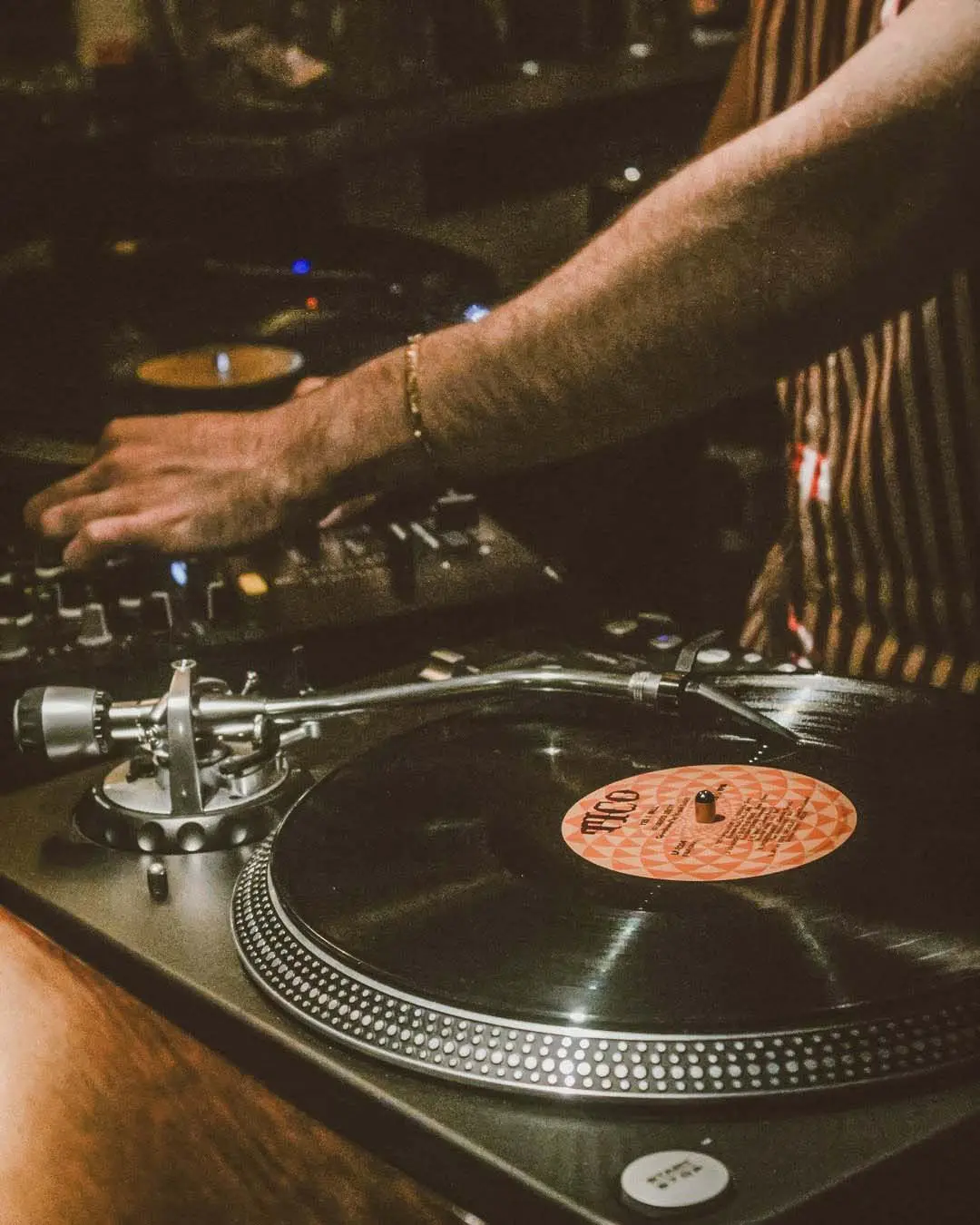 DJ's hand on mixer with a playing vinyl record, capturing the essence of a live music session