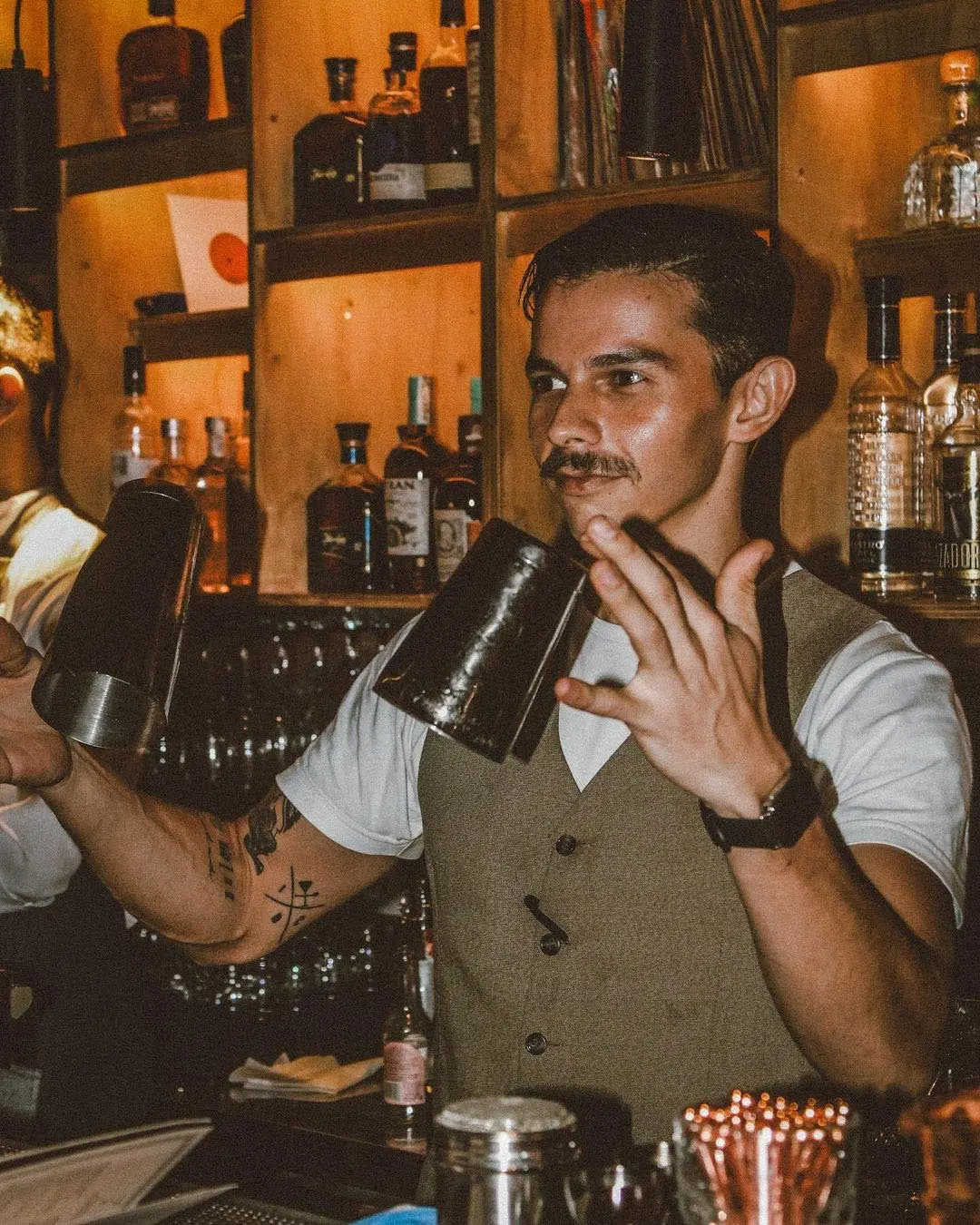 Various liquor bottles on wooden shelves, including Botran, with artwork in the background